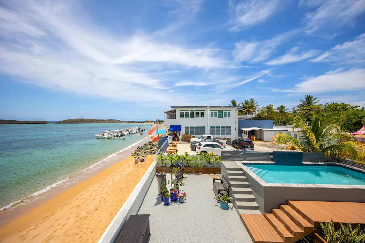 Vista aérea de la villa y su piscina directamente sobre la playa de Puerto Nuevo, con botes y la comunidad alrededor