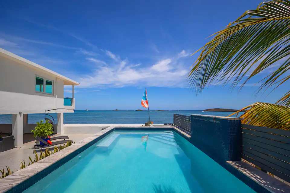 La piscina de Villa Ensueño con la bandera de Puerto Rico y el mar al fondo